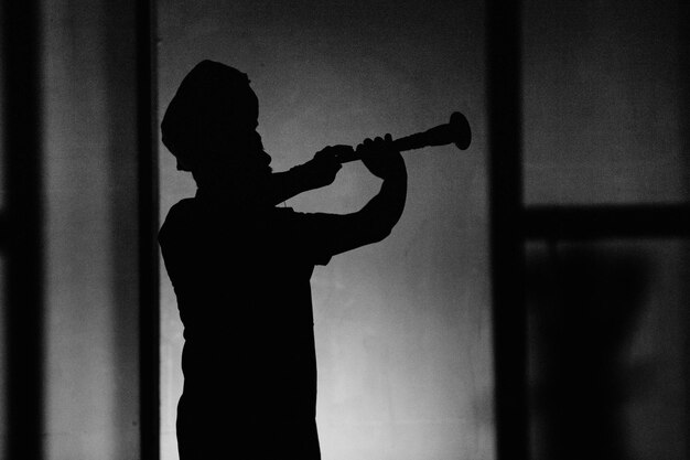 Foto silhouette uomo che suona l'oboe vicino al muro