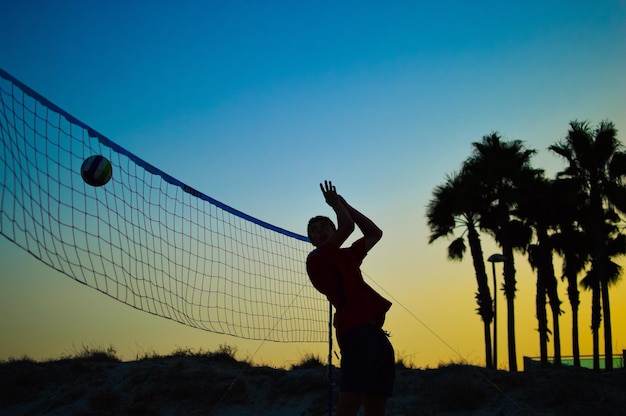 写真 夕暮れの空に向かってバレーボールをしているシルエットの男