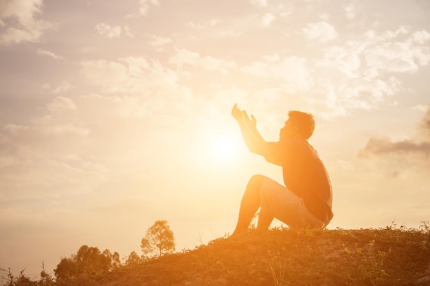 Foto silhouette uomo che prega mentre è seduto sulla terra contro il cielo durante il tramonto