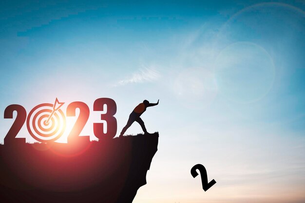 Silhouette man push number two from clip with 2023 year and blue sky for preparation new business target when change new year concept