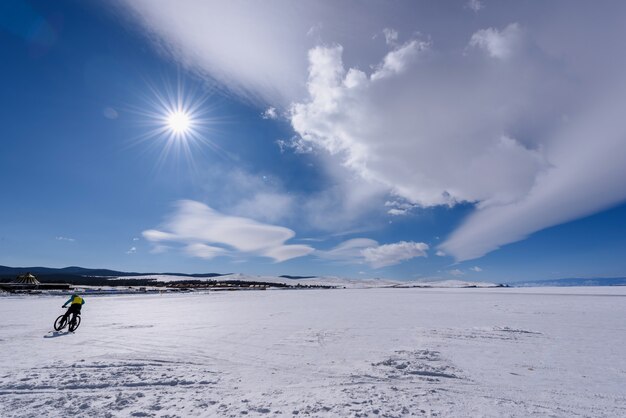 La siluetta dell'uomo guida la bicicletta sul lago baikal congelato in tempo soleggiato con il bello cielo delle nuvole