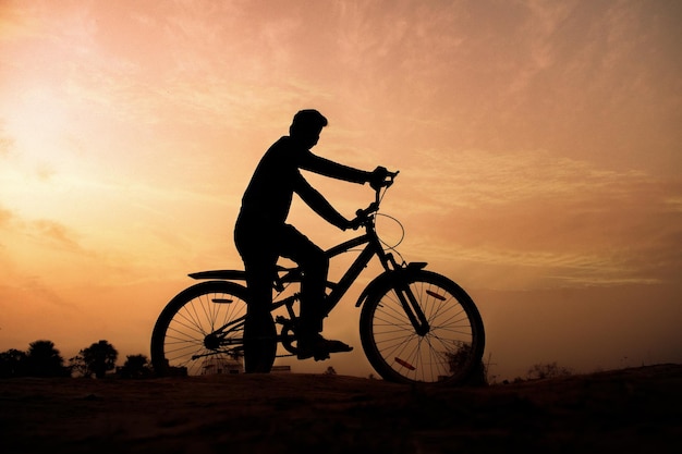 Silhouette of a man rides a bike at sunset orange sky\
background