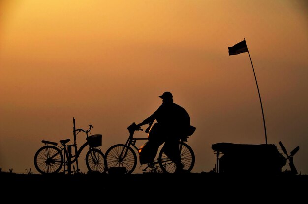 Silhouette man riding bicycle against sky during sunset