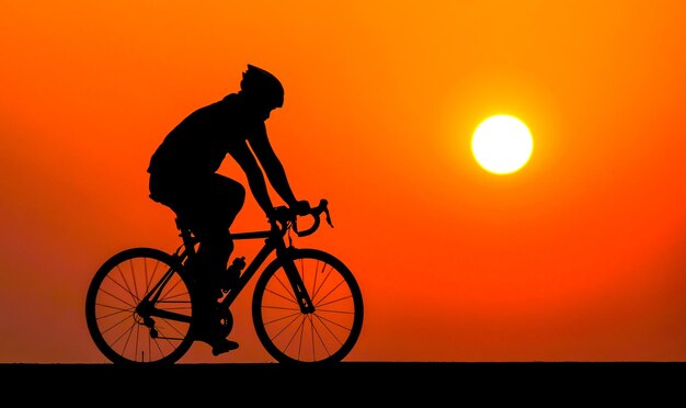 太陽とオレンジ色の空に逆らって自転車に乗っているシルエットの男性