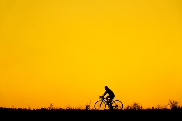 Silhouette man riding bicycle on field against orange sky