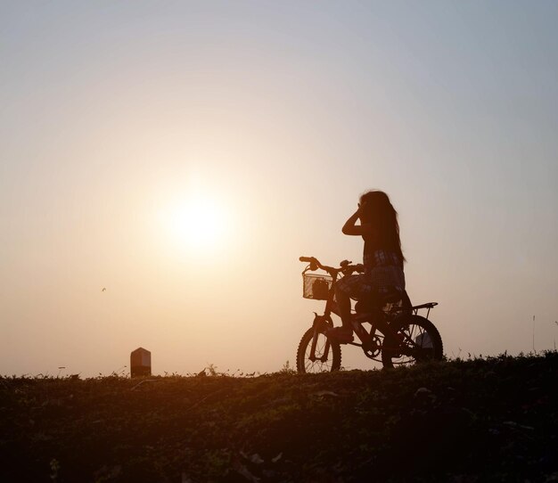 Silhouette man riding bicycle on land against sky during sunset