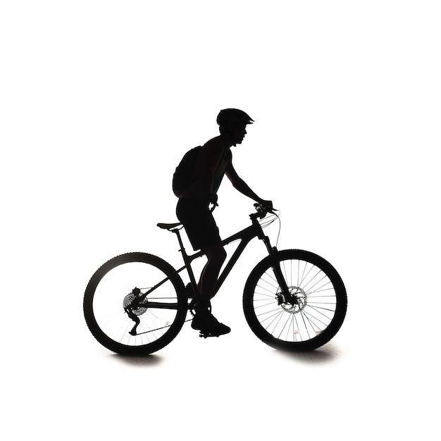 A silhouette of a man riding a bike with a backpack on it.