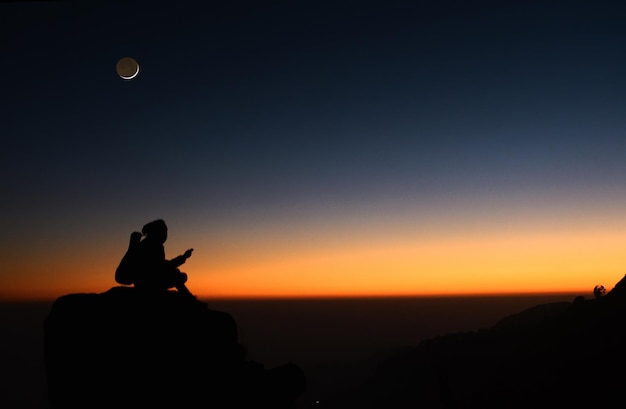 Foto silhouette di un uomo sulla roccia contro il cielo durante il tramonto