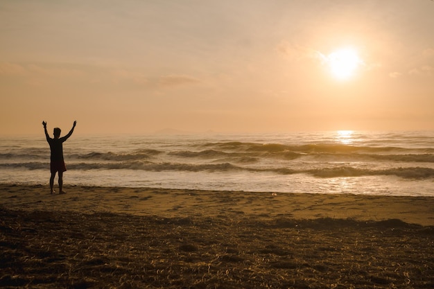 写真 日の出と海の背景でビーチで走るシルエットの男