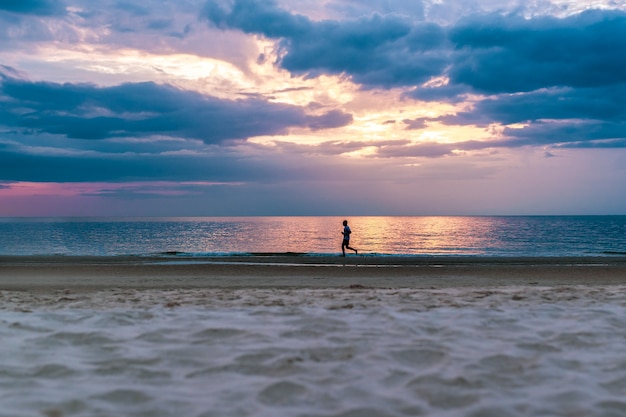 Силуэт человека работает на пляже на закате.