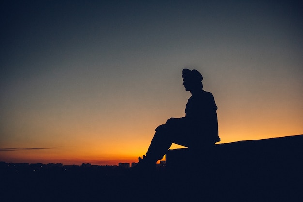 Silhouette of a man's portrait, watching the sunset over the city. Urban man with hat. Good looking.