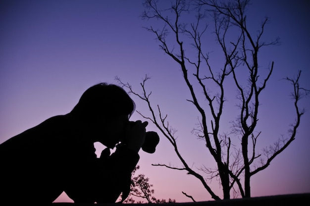 日没時に木の枝を撮影する男のシルエット