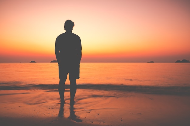 La silhouette di uomo seduto da solo in spiaggia