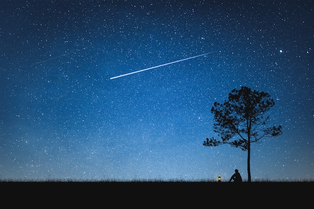 Silhouette of man sitting on mountain and night sky with shooting star. alone concept.