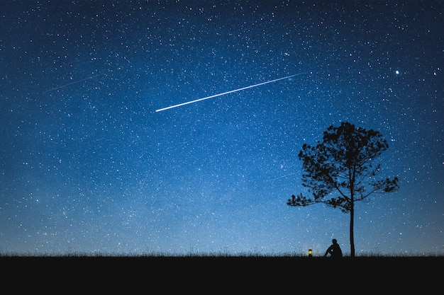 Photo silhouette of man sitting on mountain and night sky with shooting star. alone concept.