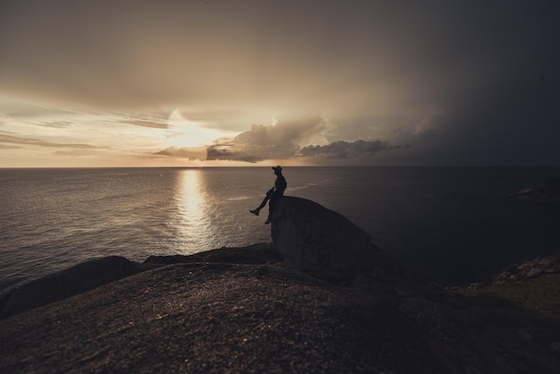 Foto silhouette di un uomo seduto su una formazione rocciosa contro il cielo durante il tramonto