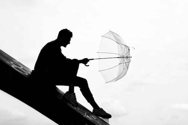 Foto uomo a silhouette seduto con l'ombrello contro il cielo