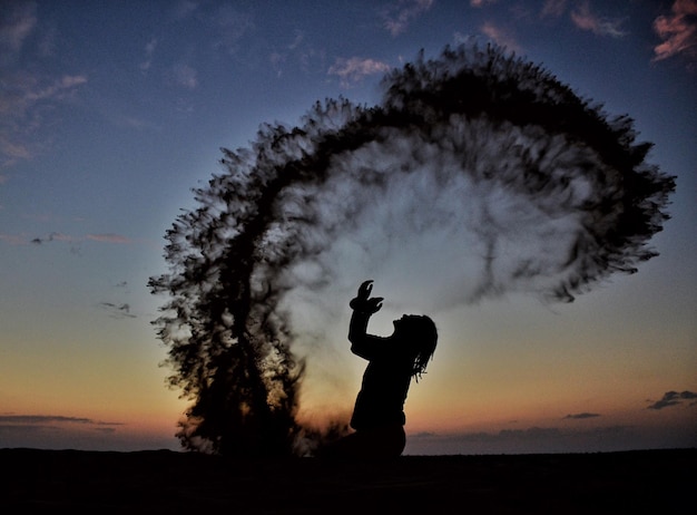 Foto uomo a silhouette che spruzza sabbia sulla spiaggia contro il cielo durante il tramonto