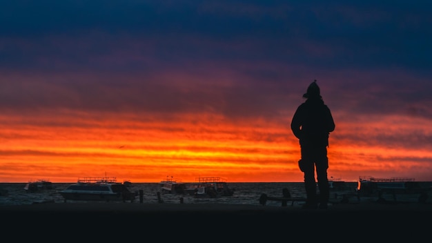 Photo silhouette man standing on beach against orange sky