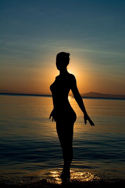 Photo silhouette man standing on beach against sky during sunset