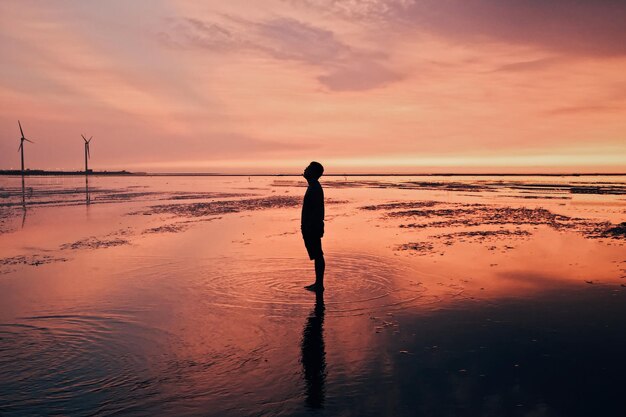 Silhouette man standing at beach against sky during sunset