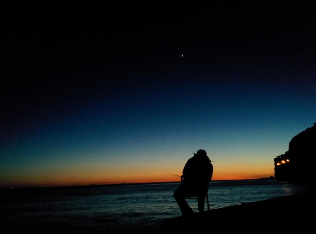 Photo silhouette man standing on beach against sky during sunset