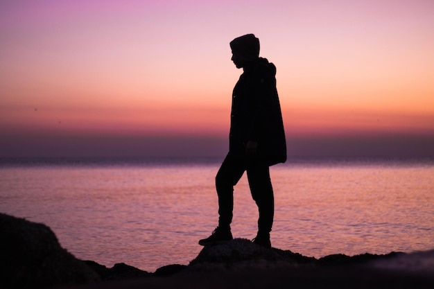 夕暮れの空に向かってビーチに立っているシルエットの男