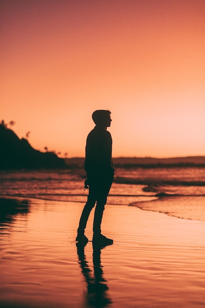 Silhouette man standing at beach against sky during sunset
