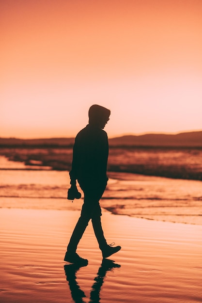 Silhouette man standing at beach against sky during sunset