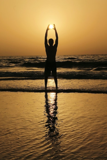 Photo silhouette man standing at beach during sunset