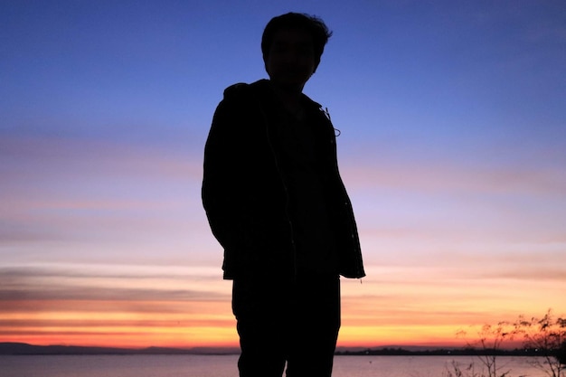 Photo silhouette man standing at beach during sunset