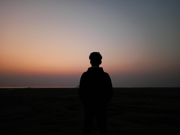 Photo silhouette of a man standing on the beach at sunset