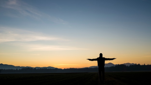 夕暮れ時に美しい風景に腕を広げて立っている男のシルエット