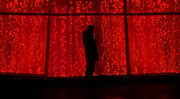 Silhouette man standing by illuminated window