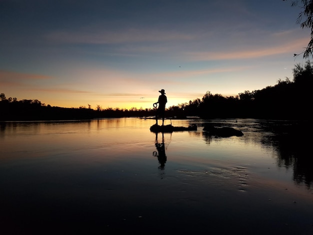 Foto silhouette di un uomo in piedi vicino al lago contro il cielo durante il tramonto