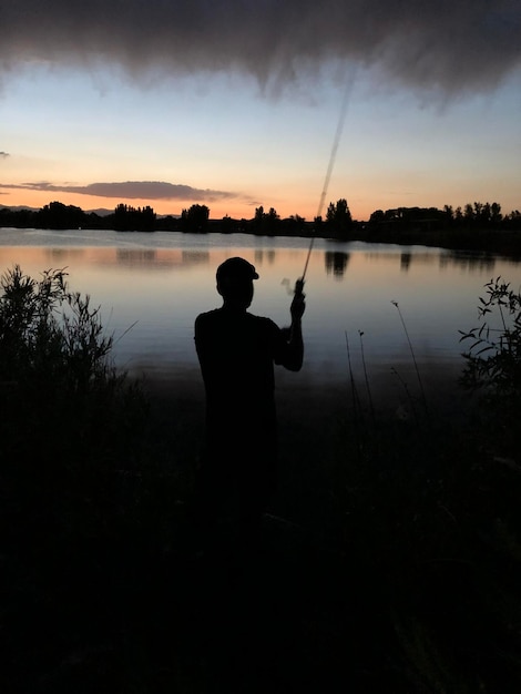 写真 夕暮れの空に逆らって湖のそばに立っているシルエットの男