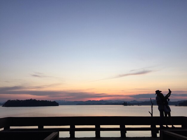 Silhouette man standing by railing against sky during sunset