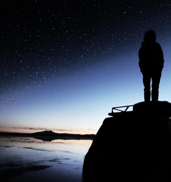 Photo silhouette man standing by sea against star field during sunset