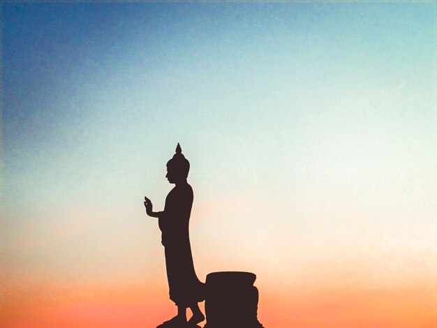 Silhouette man standing by statue against sky during sunset