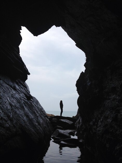 空の向こうの海の崖の上に立っているシルエットの男