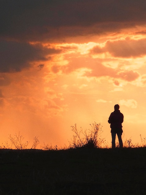 Silhouette man standing on field against orange sky