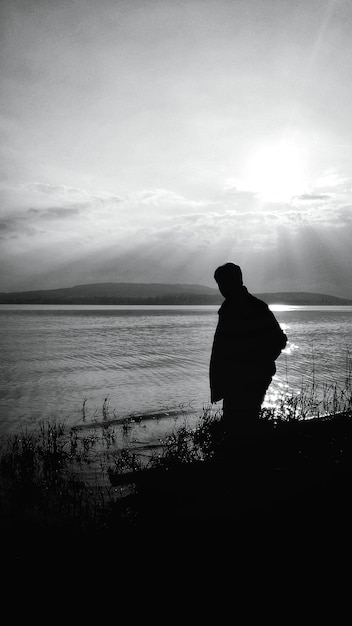 Foto uomo a silhouette in piedi sulla riva del lago contro il cielo durante il tramonto