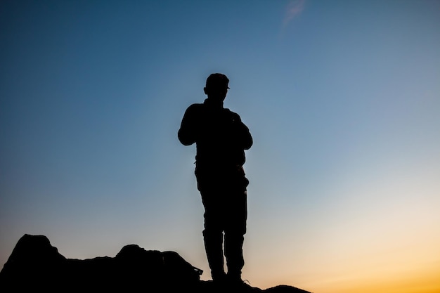 silhouette of a man standing looking at the sunset from a mountain