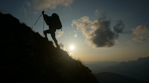 夕暮れの空に向かって山の上に立っているシルエットの男