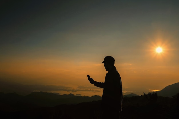 夕暮れの空に照らされた山の上に立っているシルエットの男