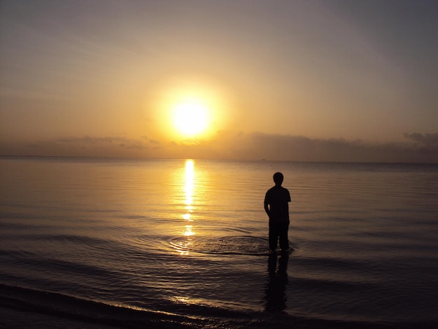 写真 夕暮れの空に向かってビーチに立っているシルエットの男