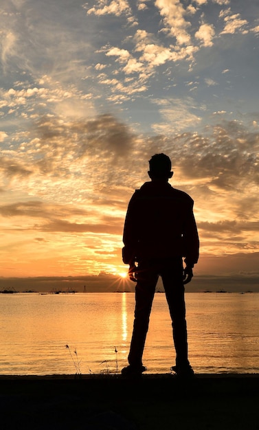사진 해가 지는 동안 하늘을 배경으로 해변에 서 있는 실루 남자