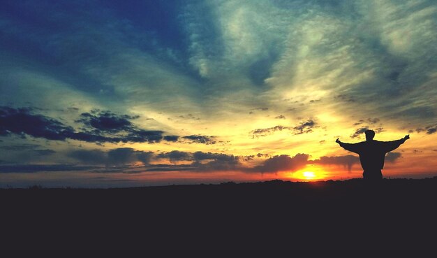 写真 夕暮れの空に照らされた風景に立っているシルエットの男