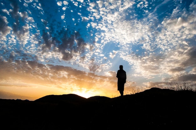 写真 夕暮れの空に向かって山の上に立っているシルエットの男