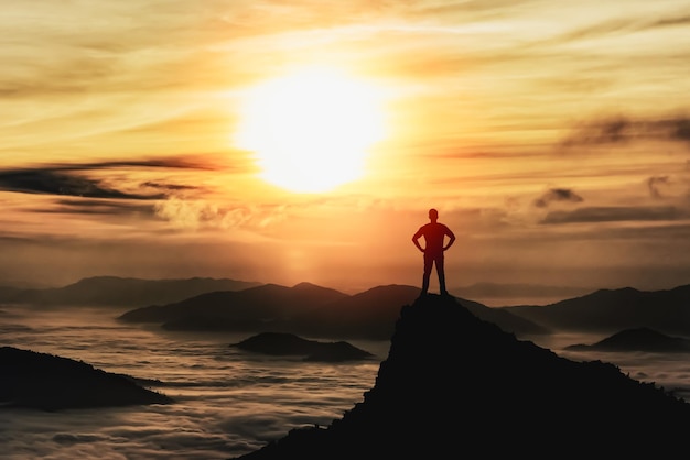 Silhouette man standing and raise two hand on peak stone rock in mountain and watching to sunrise fog mist sunset sunlight Misty valley Man hikePerson silhouette stand Mountain nature concept